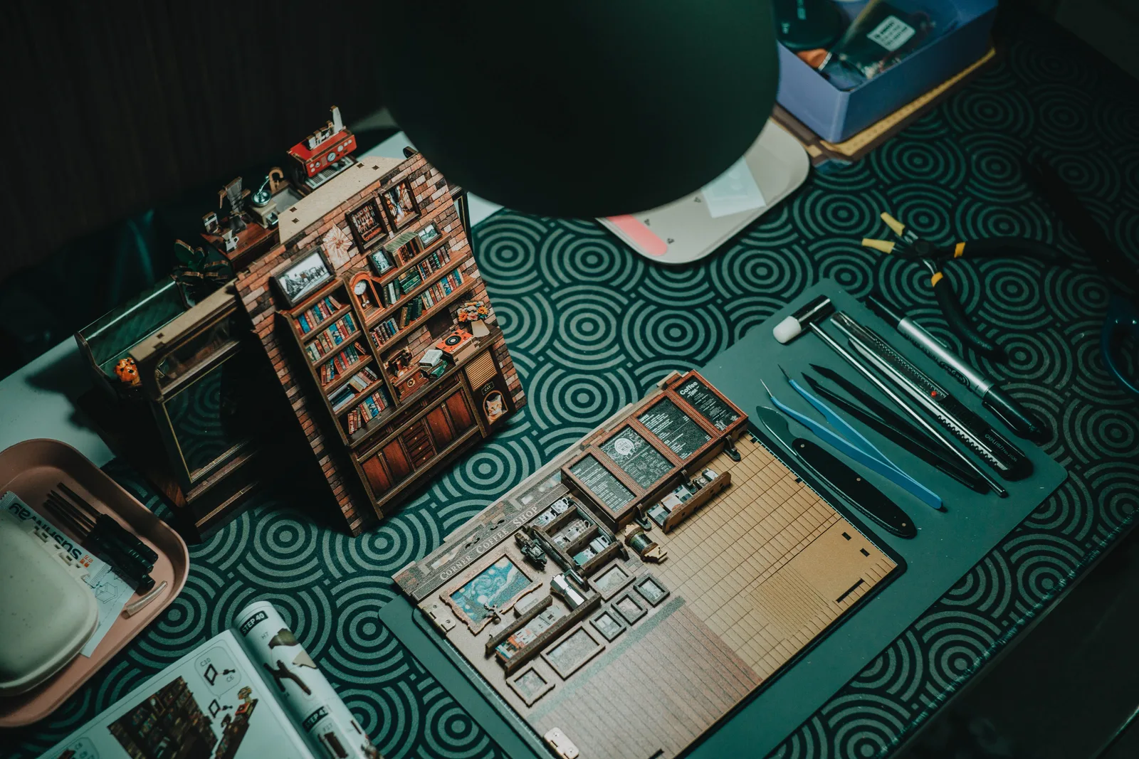 A detailed miniature bookshelf crafting setup with tools on a patterned table. Fitting a book nook kit workspace into one shared room