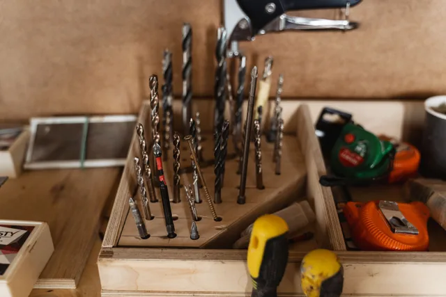 A detailed view of assorted drill bits and carpentry tools neatly stored in a wooden organizer. A kitchen table book nook workbench: tray, fumes, storage and pack down