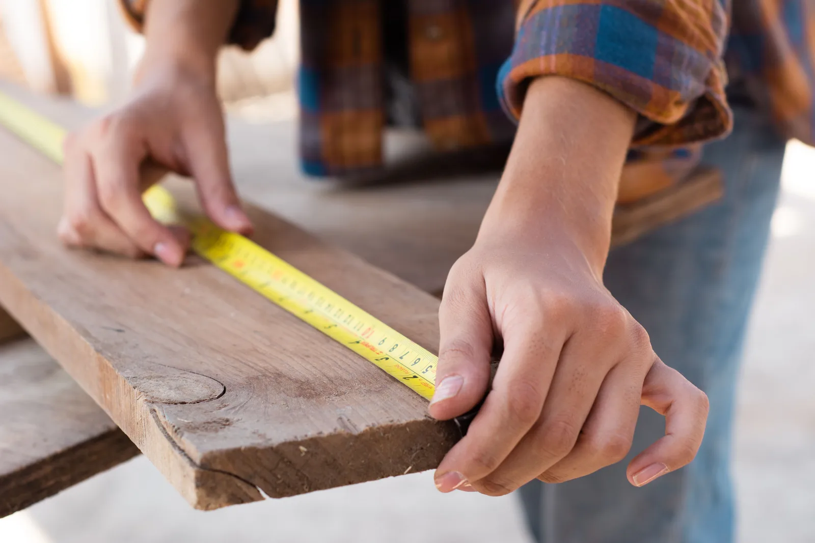 Close-up of hands measuring a wooden plank with a tape measure in a carpentry setting. Proportion and restraint: what miniature room ideas actually demand